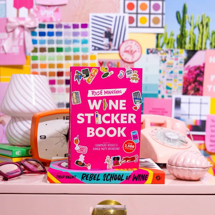 The Wine Sticker Book set down on a pink dresser in front of the Rebel School of Wine book